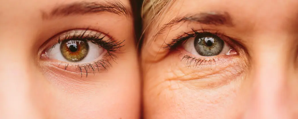 На изображении два глаза, один из которых коричневый, а другой - голубой. Глаза расположены рядом и отражают живую эмоциональную связь между двумя людьми. Кожа вокруг глаз свидетельствует о возрасте, создавая контраст между юностью и зрелостью.
